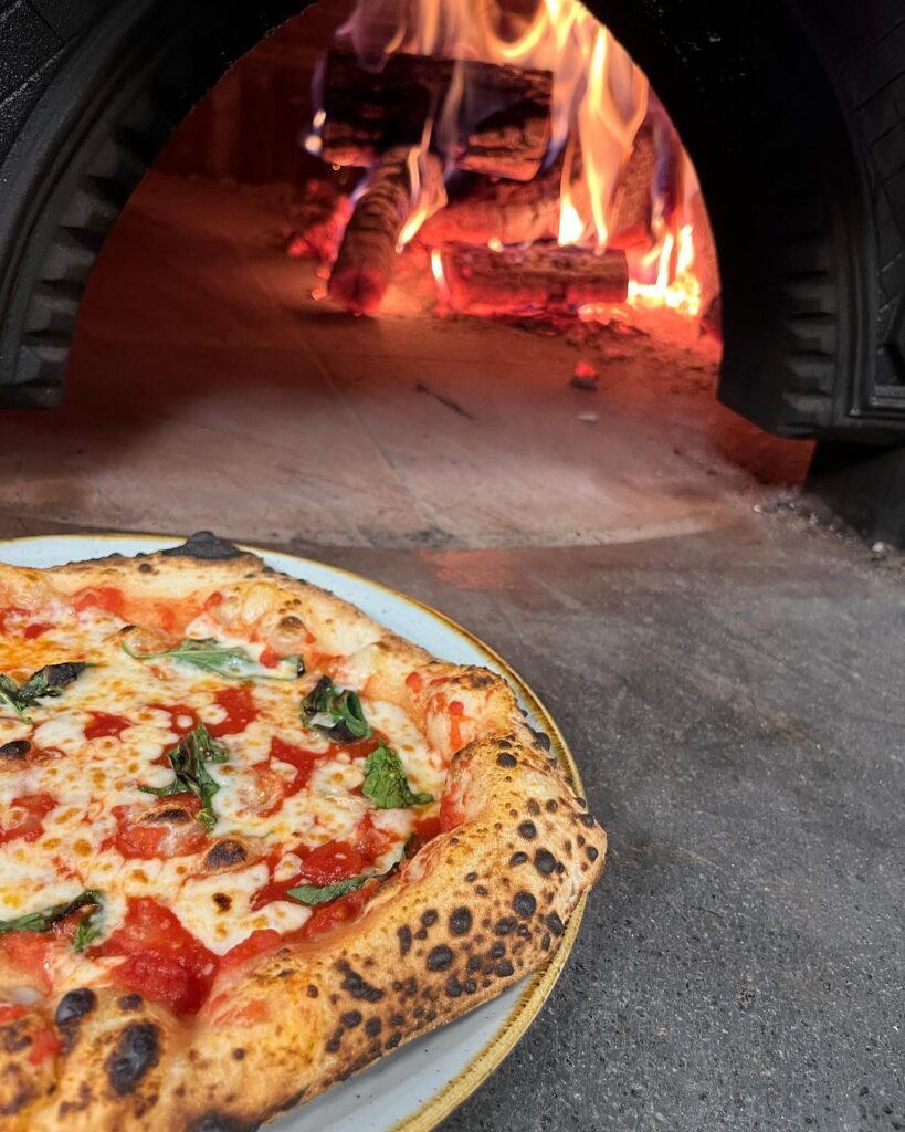 Pizza Margherita foran brændefyret stenovn