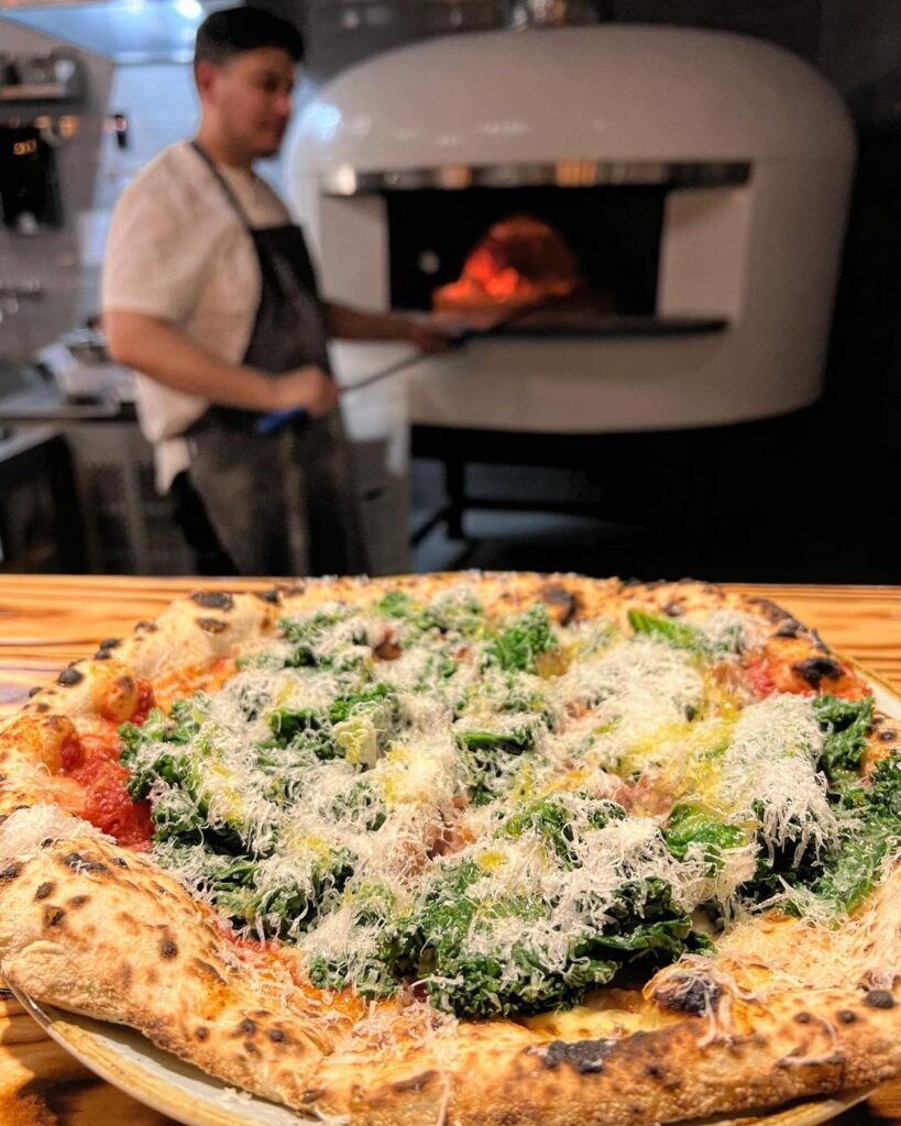 Pizza med grønkål og revet ost foran stenovn