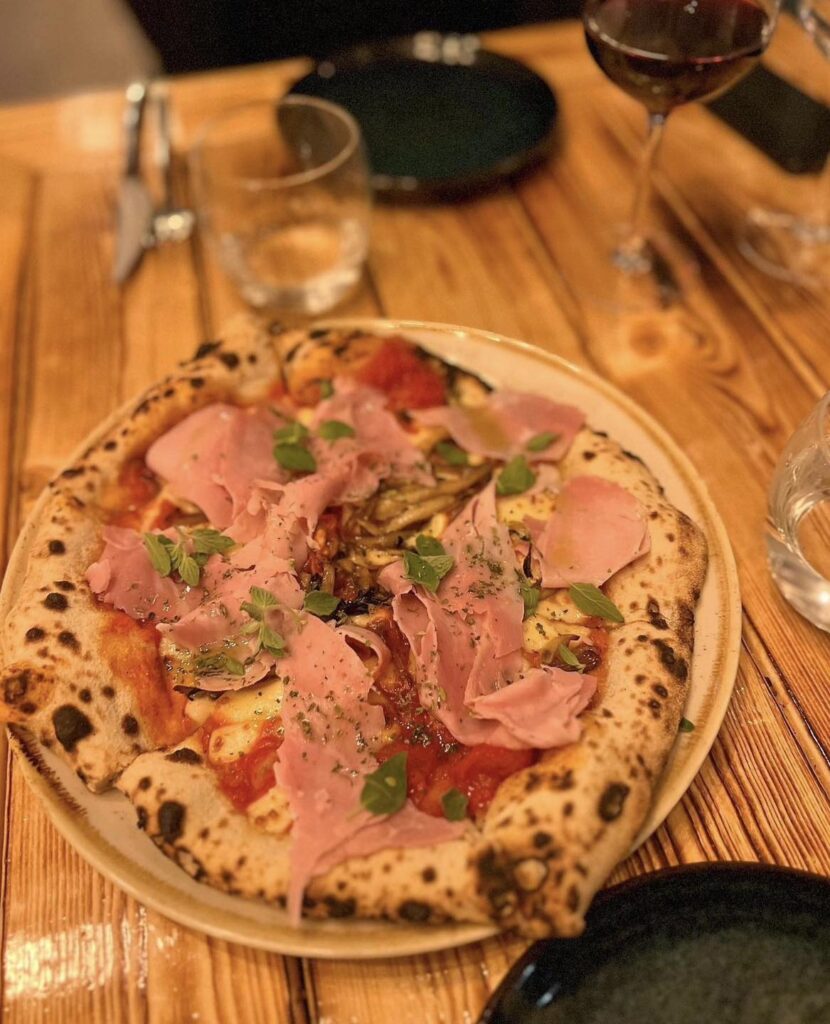 Pizza med skinke og friske urter på bord