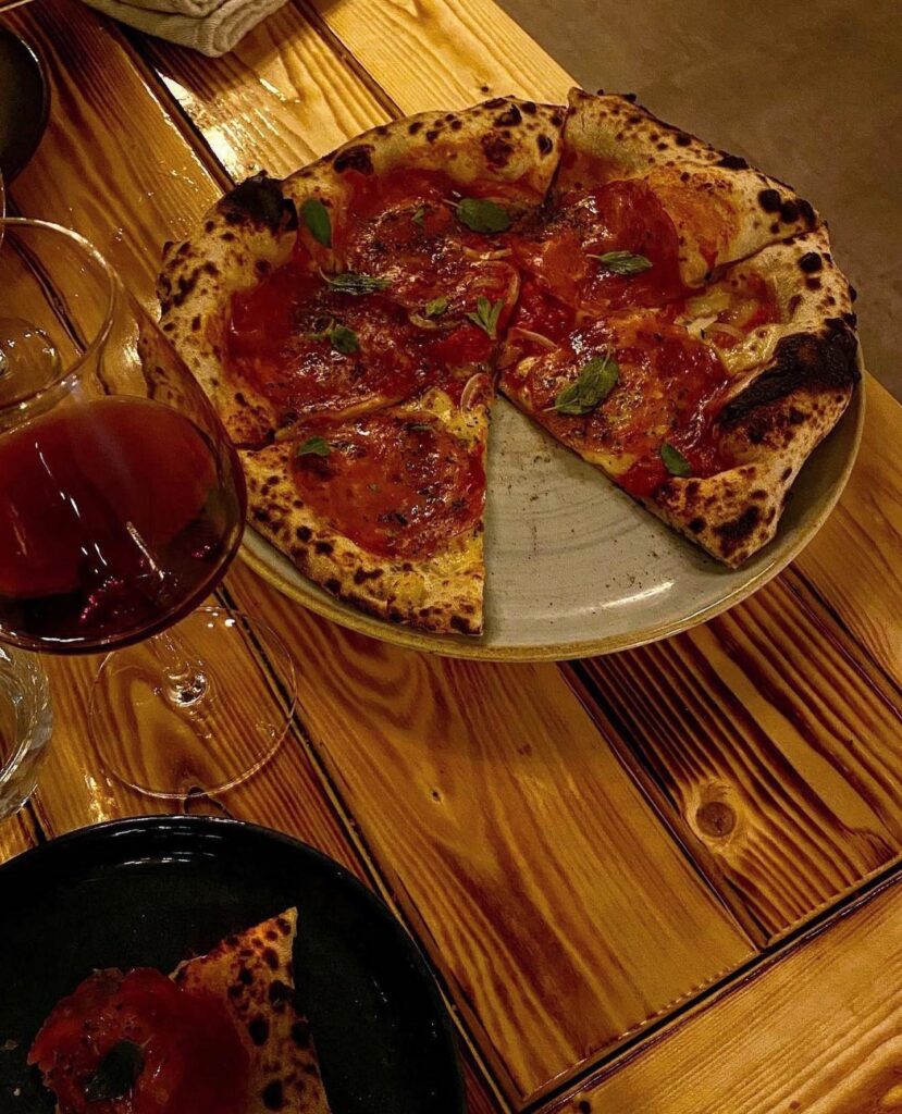 Pizza med tomatsauce og basilikum på træbord